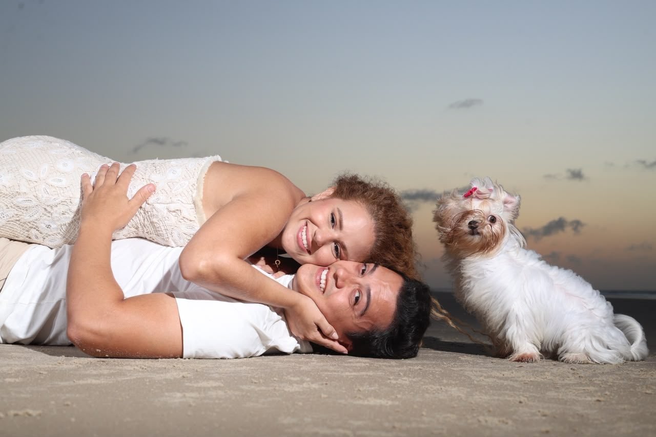 Casal deitado na areia com seu cachorro
