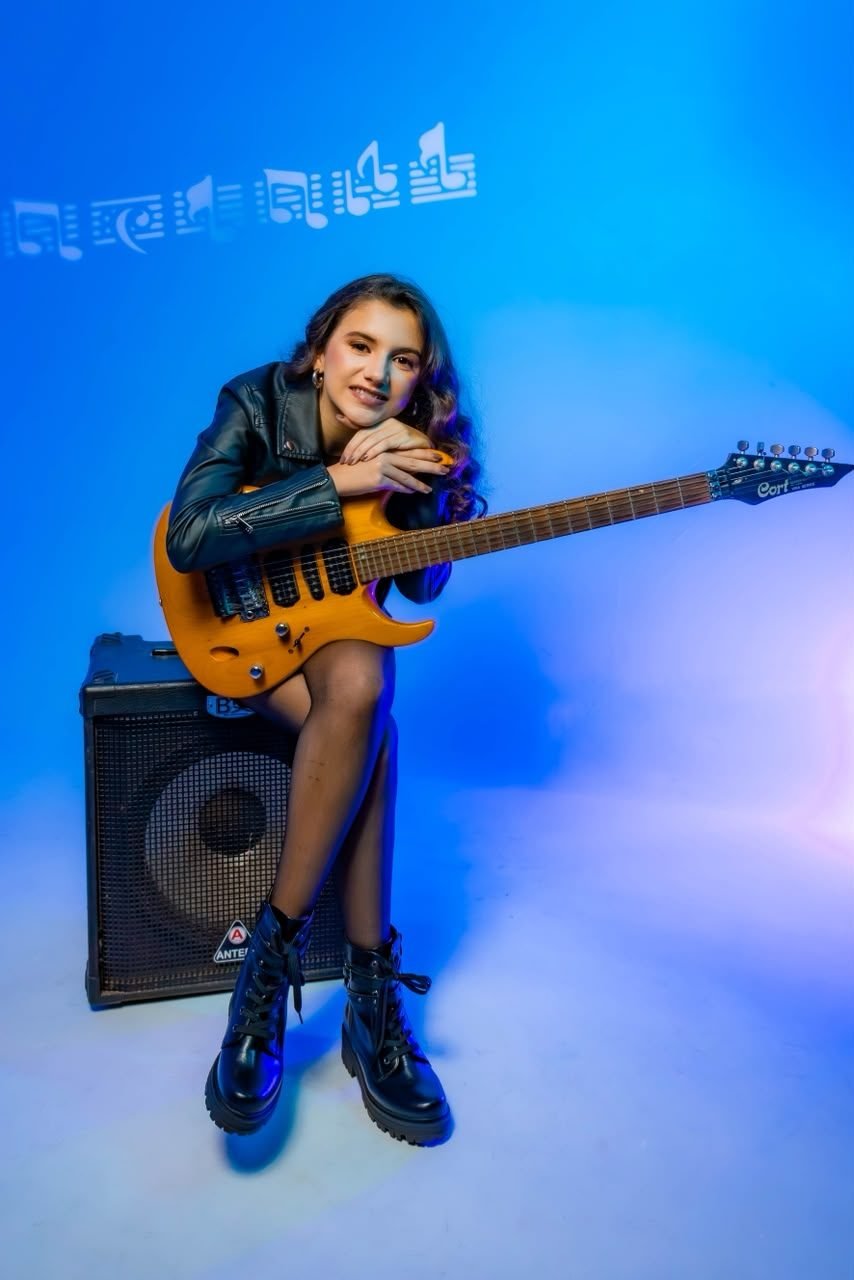 Jovem com guitarra sentada em amplificador, fundo azul